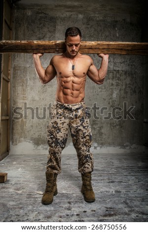 Man in army pants with naked torso holding board on his shoulders