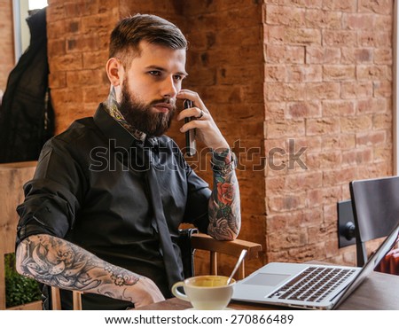 Handsome modern man calling by smartphone and working with laptop. Cafe interior.