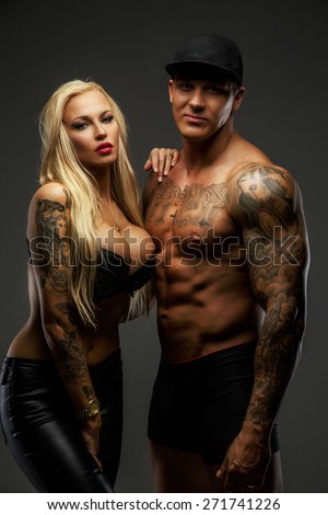 Modern couple with tattooed bodies posing in studio