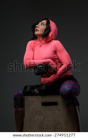 Attractive fitness woman in sportswear posing with dumbells in sudio on grey background