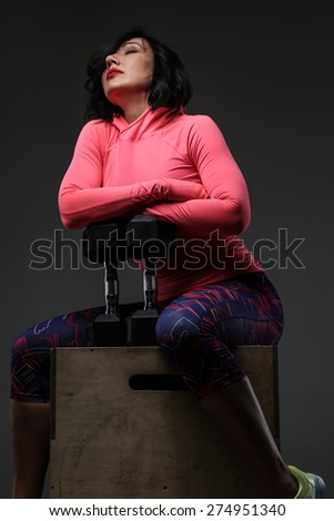 Attractive fitness woman in sportswear posing with dumbells in sudio on grey background