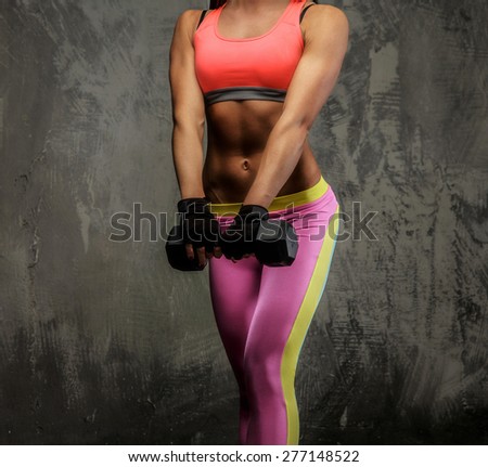 Fitness woman in colorful sportswear holding dumbell and posing in studio on grey background