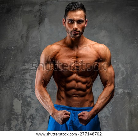Muscular guy showing his muscles. Grey background