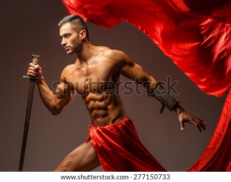 Shirtless male in roman armor with sword in motion. Red cloth on grey background