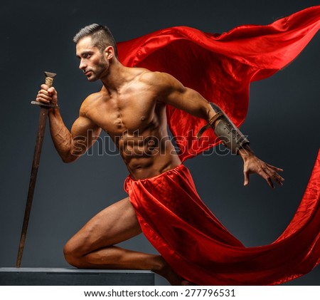 Shirtless male in roman armor with sword in motion. Red cloth on grey background