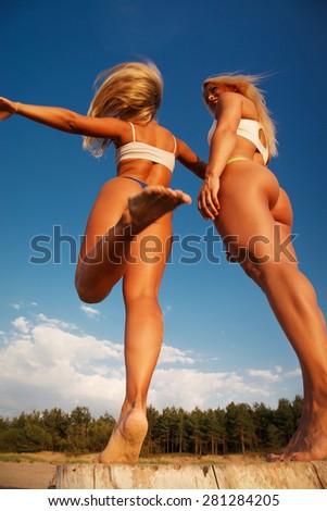 Two girls from a back in sexy swimsuits on a beach under blue sky
