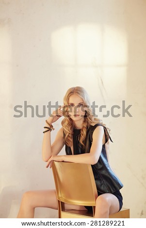 Blond woman in black clothes sits on a chair in light room