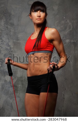 Fitness woman in sportswear doing exercises with expander on grey background