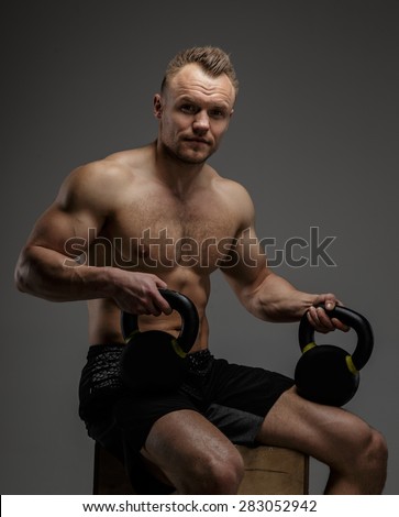Muscular guy in black shorts sitting on podium and doing exercises with weights