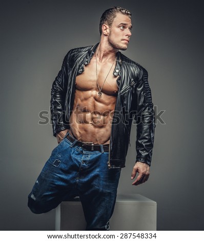 Muscular male in blue jeans and black jacket wearing on shirtless body. Isolated on grey background.