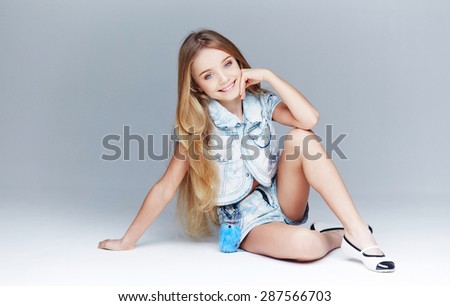 Little girl model with long hair and blue eyes posing on light grey background.