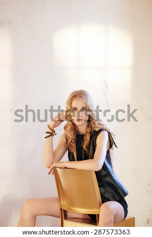 Blond female posing on chair in studio.
