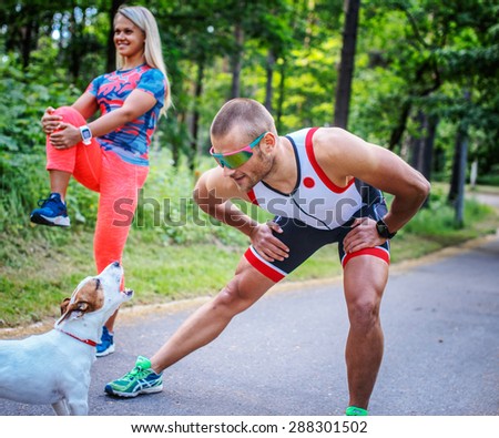 Man and woman in sportswear doing exercises and their dog on the forest road.