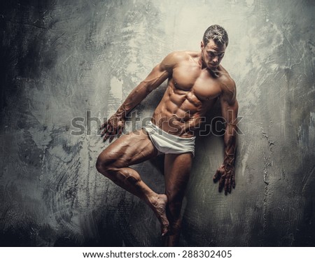 Muscular fitness model guy in white panties posing on grey background.