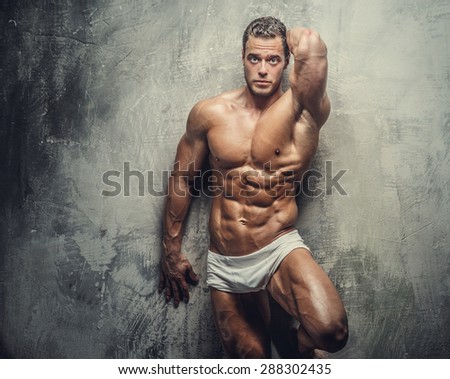 Muscular fitness model guy in white panties posing on grey background.