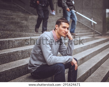Serious guy in casual clothes sitting on steps.