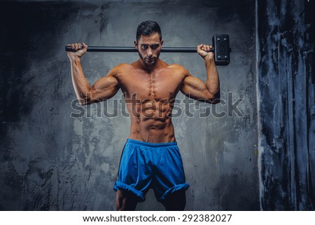 Shirtless muscular fitness man holding big hummer behind his head.