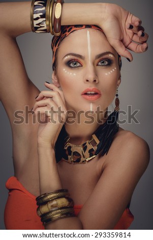 Portrait of woman with exotic make up. Bracelets on hands and orange leopard pattern on bandana.