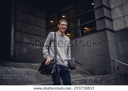 Man in casual clothes holding laptop and posing on modern street.