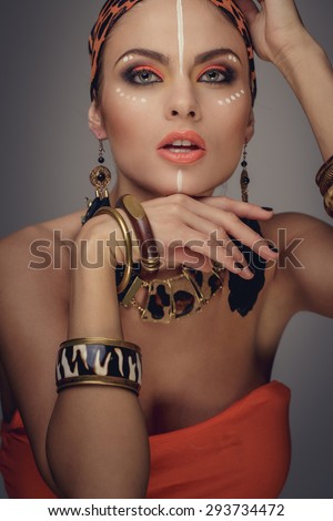 Attractive woman with exotic make up posing on camera with hands near her face.