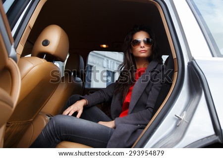 Casual female with long black hair in sunglasses sitting in the car on back seats.