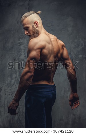 Muscular guy from back posing in dark shadows over grey background.