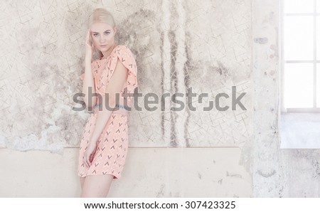 Slim fashion blond model in pink dress posing over light grey background.