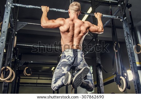Shirtless man pulling up on horizontal bar in a gym.