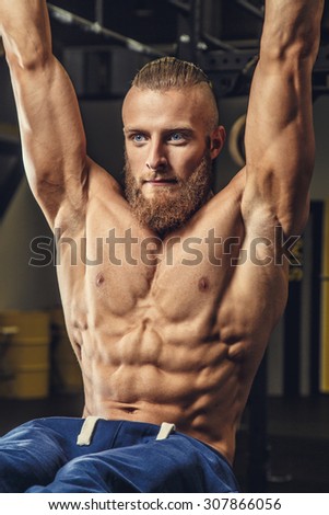 Shirtless muscular guy with beard doing exercises in a gym.