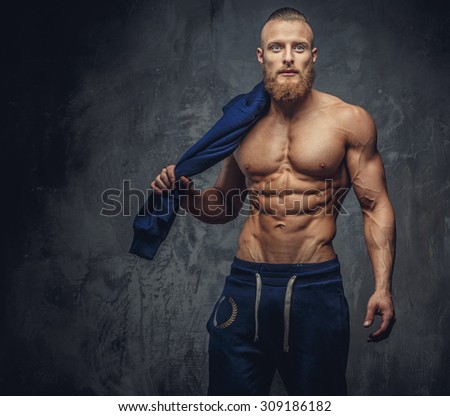 Portrait of muscular guy with beard in blue sports pants isolated on grey background.