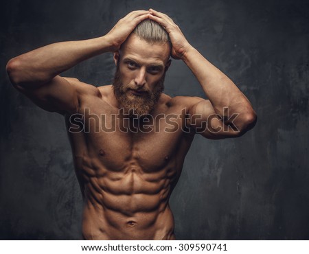 Shirtless muscular man with beard holding his hands to the head over grey background.