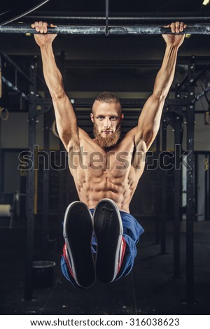 Bodybuilder with beard doing pull ups on horizontal bar in a gym.