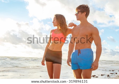 Couple of muscular man and sporty woman posing on the beach over sky with white clouds.