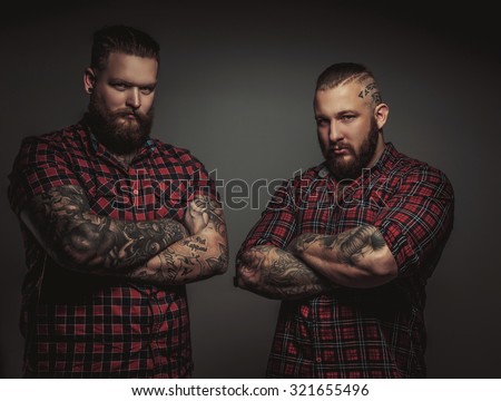 Two brutal mans with beards and tattoo isolated on grey background. Crosed arms.