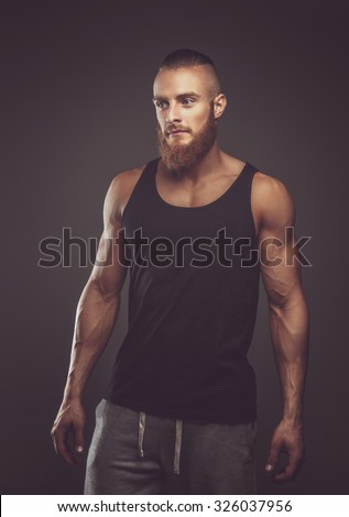 Athletic bearded man in black t shirt over dark background.