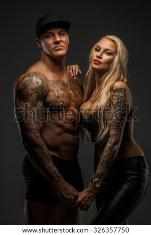Muscular tattooed man and his blond sexy woman isolated on grey background.