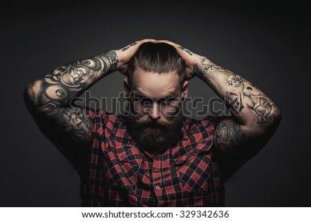 Mans with beard and tattoes on arms holding his head. Isolated on grey background.