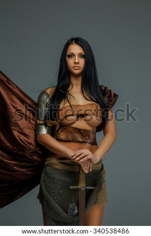 Sexy brunette woman in ancient  roman armor holds sword. Isolated on grey background.