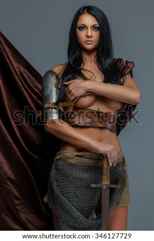 Sexy brunette woman in iron armor posing on grey background.