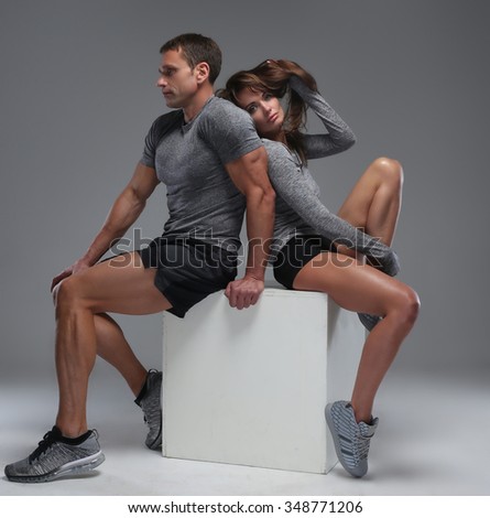 Fitness man and woman sit on white box in studio over grey background.