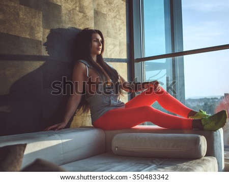 Attractive brunete woman in red sports pants posing near window.