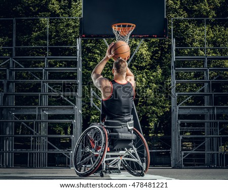 Cripple basketball player in wheelchair plays basketball on open air ground.