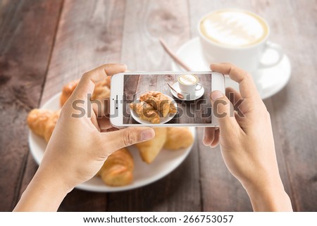Taking photo of fresh baked croissants and coffee on wood table.