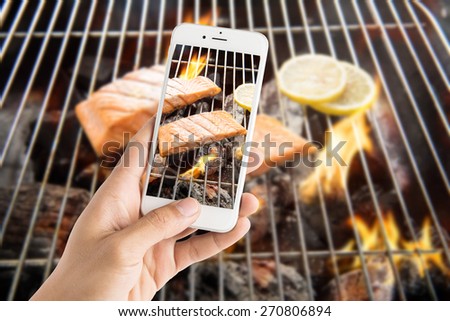 Taking photo of grilled salmon with lemon on the flaming grill