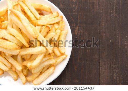 French fries on white dish on wooden background.