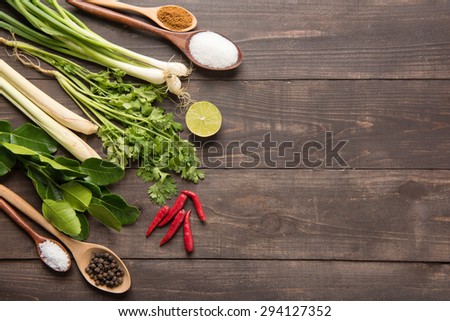 Kaffir lime leaves, coriander or cilantro, lemon, lemon grass, red chilli, green onions and spices on wooden background. Overhead view.