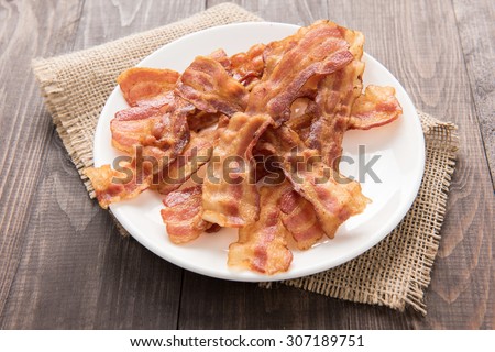 Closeup of fried bacon strips on white plate.