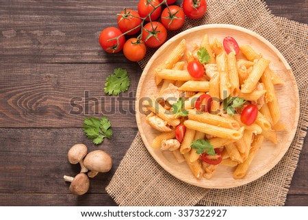 Penne pasta in tomato sauce with chicken on a wooden background.