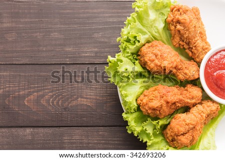 Fried chicken drumstick and ketchup on wooden background.