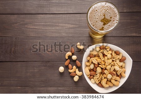 Glass of beer and almond, macadamia, peanut, cashew nut on the wooden background.